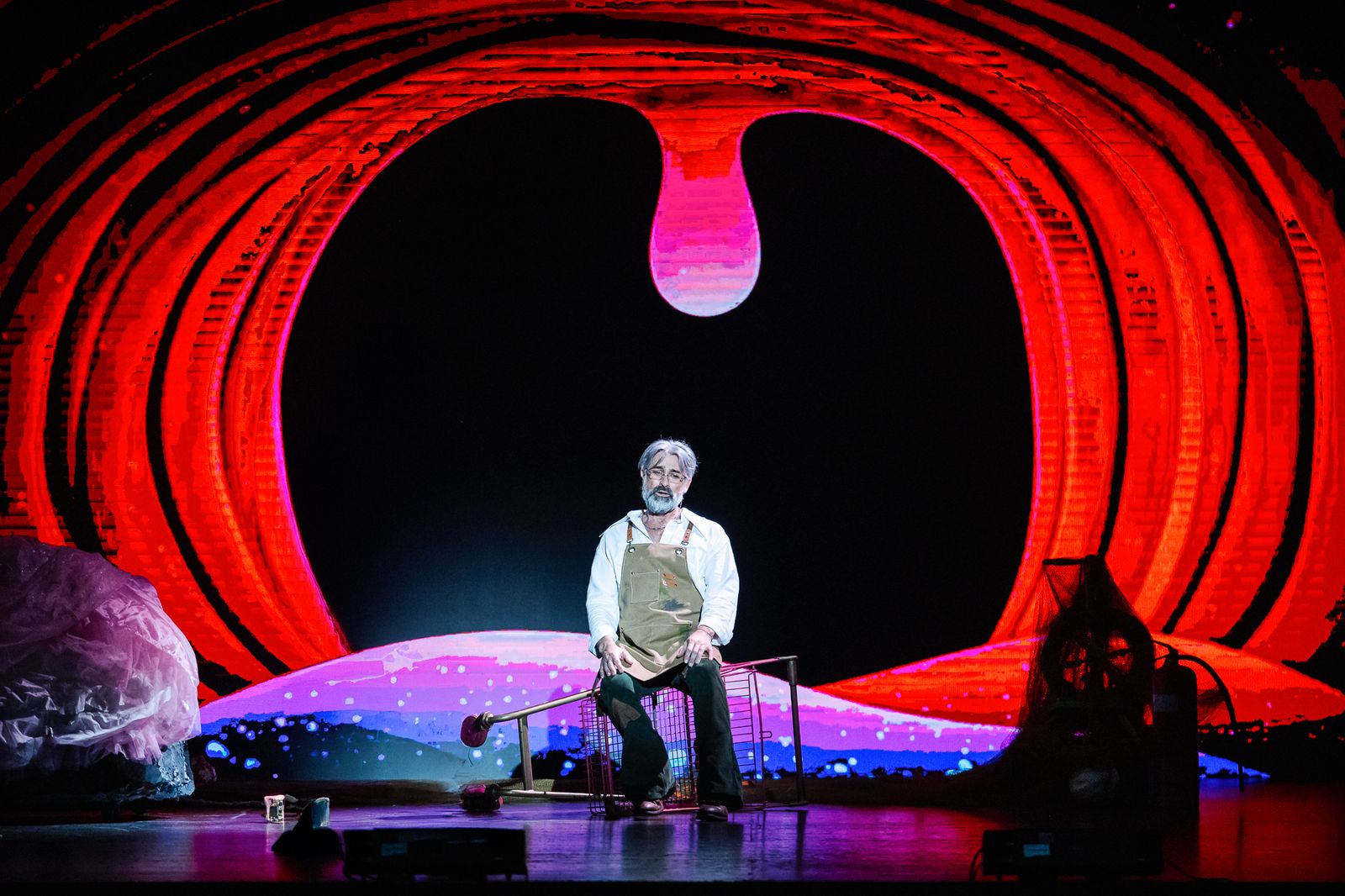 Geppetto on a stool in front of a giant red stage set, Pinocchio pantomime by Zealous Productions, December 2024