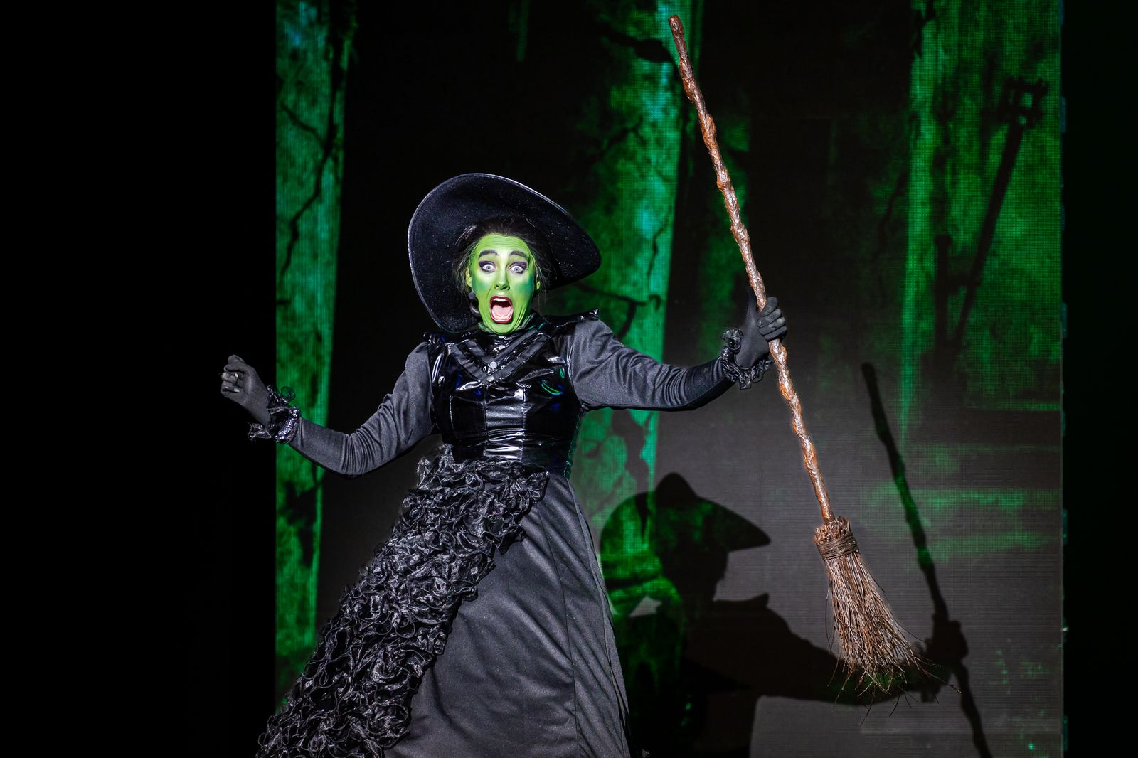 The green-faced Wicked Witch of the West with her broomstick, The Wizard of Oz pantomime by Zealous Productions, December 2025
